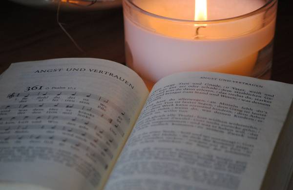 Quelle: EKHN/Matern / fundus-medien.de, Fundus, redaktionell frei verwendbar, 207 Aufgeschlagenes Evangelisches Gesangbuch mit Nummer 361; dahinter brennt eine weiße Kerze.